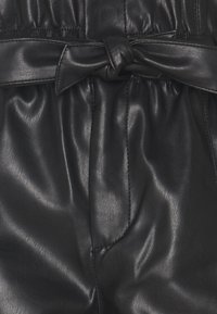 Närbild av en svart läderplagg med ett knytet bälte och synlig sömnad på den rynkade tyget.