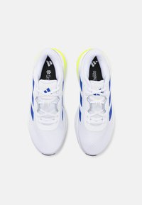 White athletic shoes with blue stripes, mesh upper, cushioned soles, and black insoles featuring "Ortholite" branding. Neon yellow accents visible.