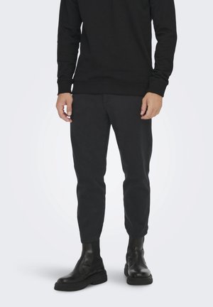 Sudadera negra de manga larga, pantalones ajustados negros y elegantes botas negras hasta el tobillo. Mezcla de algodón con textura suave, diseño minimalista.