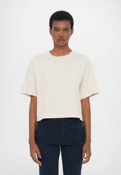 T-shirt accorciato a coste in cotone bianco sporco. Presenta un collo rotondo e maniche corte, abbinato a pantaloni blu scuro.