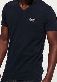 Marineblauw V-hals T-shirt gemaakt van zachte katoen, met een klein rood en wit logo op de linkerborst en korte mouwen.