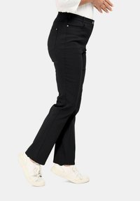 Zwarte stretchbroek met een elastische tailleband, slim fit, voor- en achterzakken en stikseldetails. Gepaarde met witte sneakers.
