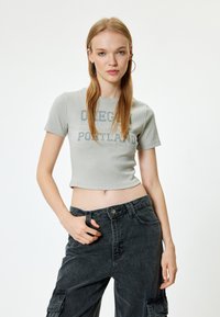 Harmaa ribbattu lyhythihainen crop-top, jossa on painatus, jossa lukee "Oregon Portland". Yhdistetty tummiin, rentoihin cargo-housuihin.