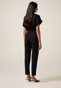 Zwarte, kortekorte mouw top en slanke zwarte broek, aangevuld met zwarte slingback hakken met een spitse neus en een kleine hak. Glad oppervlak.