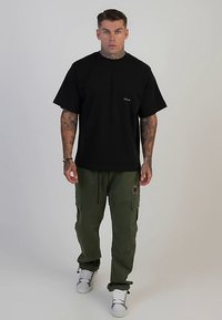 Črna oversized majica s kratkimi rokavi z majhnim logotipom, združena z olivno zelenimi cargo hlačami z žepi in obrabljenimi detajli. Bele superge.