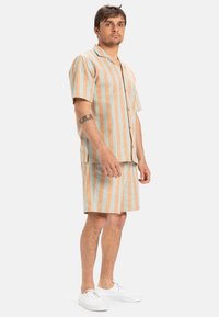 Korte mouwen shirt en bijpassende shorts in lichtbruin en blauwe verticale strepen, gemaakt van een textuurstof, gecombineerd met witte sneakers.