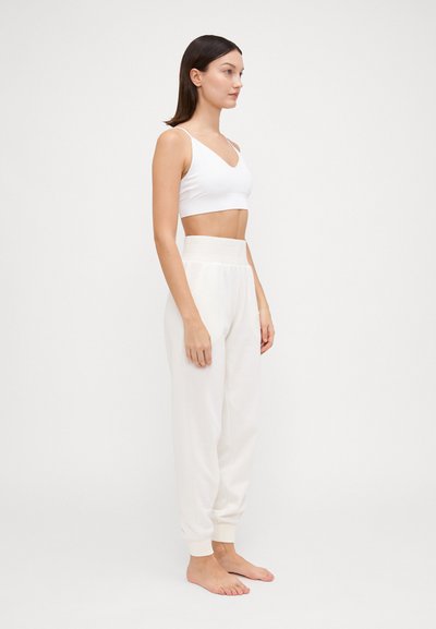 Top corto bianco senza cuciture con spalline sottili abbinato a pantaloni della tuta beige a vita alta e a gamba tapered, dotati di polsini elasticizzati e di una morbida texture.