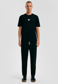 Zwarte katoenen T-shirt met een ronde hals, met een klein logo op de borst, gecombineerd met zwarte relaxte broek en zwarte sneakers.