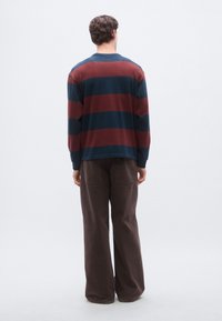 Το πουκάμισο με μακριά μανίκια έχει οριζόντιες ρίγες σε ναυτικό μπλε και βουργουνδί, στρογγυλή λαιμόκοψη και άνετη εφαρμογή· συνδυάζεται με καφέ παντελόνια φαρδιάς ίνας.