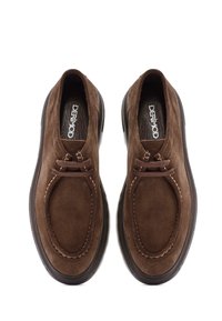 Chaussures en suéde marron sans lacets avec un bout rond, doublure en cuir, couture décorative et semelle en caoutchouc texturisée. Logo de la marque visible à l'intérieur.