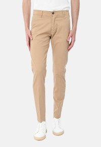 Chino in cotone beige con una vestibilità slim, dotati di chiusura a bottone, tasche laterali e una texture liscia, abbinati a sneakers bianche.