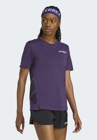 Camiseta atlética morada de manga corta con paneles laterales de malla transpirable, que cuenta con un cuello redondo y un logo de TERREX en el pecho.