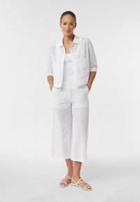 Weißes Kleidungsset aus Lochstickerei, bestehend aus einem kurzärmeligen Button-Up-Hemd, einem Tanktop und weiten Hosen; zeichnet sich durch offene Muster und einen kurzen Schnitt aus.