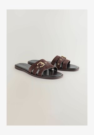 Smeđe suede sandale s ravnim potplatima, s dva široka remena s zlatnom kopčom i rupicama, na crnom potplatu s glatkom teksturom.