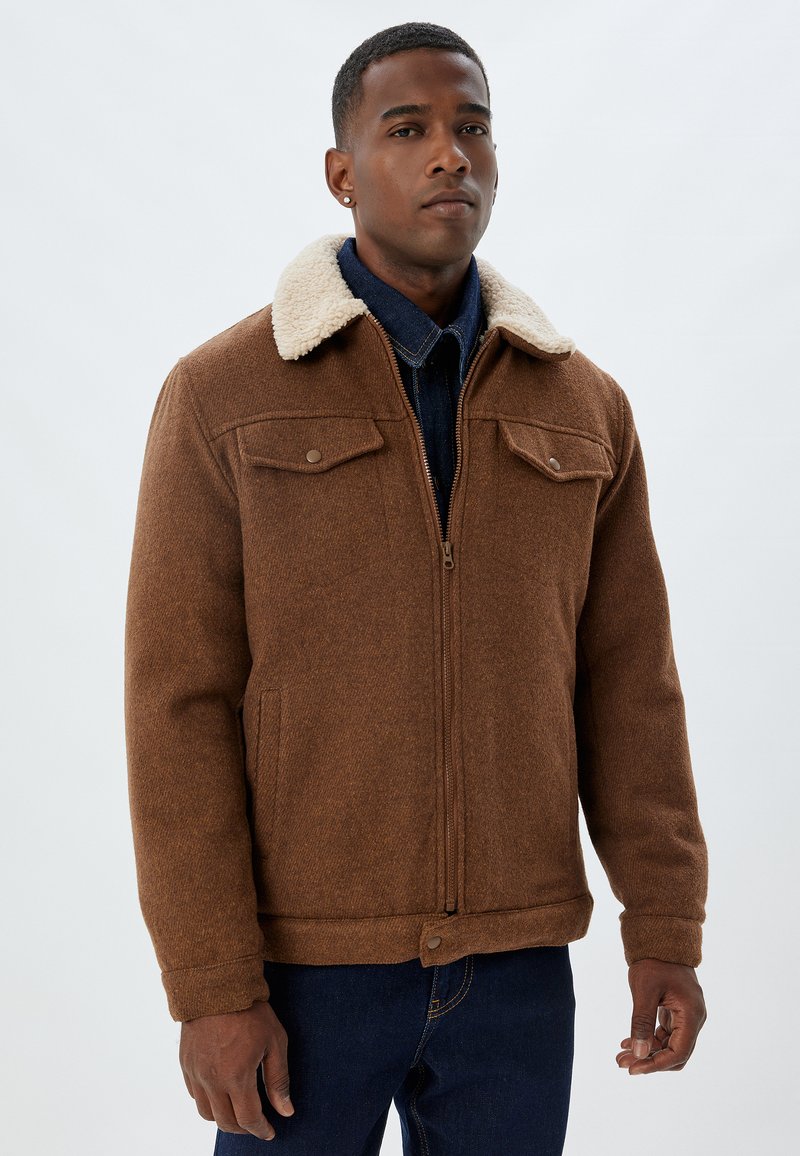 Brown wool blend jacket with a sherpa collar, zip closure, and two chest pockets. Textured fabric with a buttoned hem and cuffs.