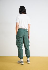 Green cargo pants with an elastic waistband and cuffs. The design features multiple side pockets, complemented by a light t-shirt and sneakers.