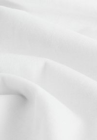 Fehér pamutszövet, puha, bordás textúrával, finom redőkkel és ráncokkal, amelyek kiemelik könnyű és sima felületét.