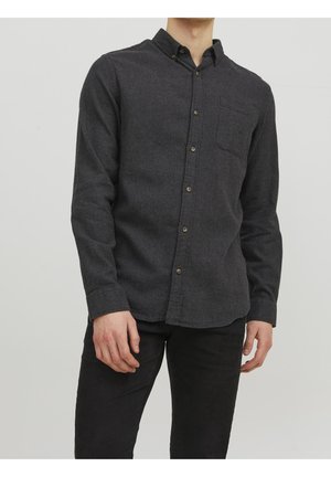 Man wearing a dark gray button-up long-sleeve shirt with a chest pocket, paired with black pants, standing against a plain background.