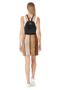 Black leather backpack with adjustable straps, rectangular shape, and a metal loop accent. The background features a brown and beige skirt.