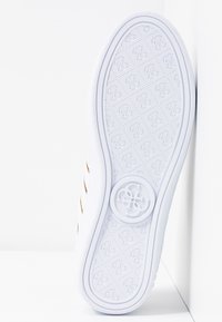Semelle blanche de basket avec motif texturé et logo circulaire au centre, photographiée sur un fond blanc d'angle.