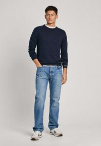 Laivasto sininen crewneck villapaita, jossa on ribbad huput, vaaleansiniset suoralahkeiset farkut ja valkoiset lenkkarit mustilla yksityiskohdilla. Yksinkertainen ja rento asu.