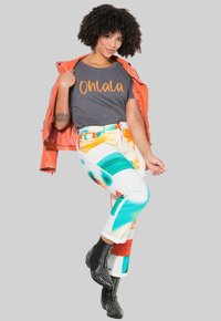 Camiseta gris con "Onlala" en naranja, chaqueta naranja, jeans de patrones coloridos en tonos turquesa y rojo, y botas negras con tachuelas en los tobillos.