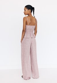 Pink striped peplum top with thin straps, paired with wide-leg pants. Fabric appears light and textured. Pockets are visible in the pants.