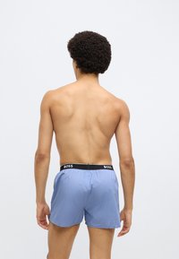 Herre badeshorts i lyseblå, laget av lettvektstoff. Har svart elastisk midjebånd med "BOSS"-merke. Kort, fleksibelt design.