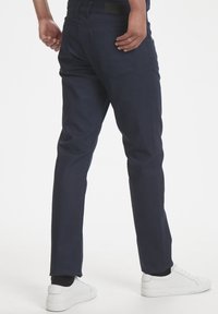 Vaqueros de corte ajustado en azul marino, hechos de mezclilla, con un diseño clásico de cinco bolsillos y una textura suave. Llevados con zapatillas blancas.