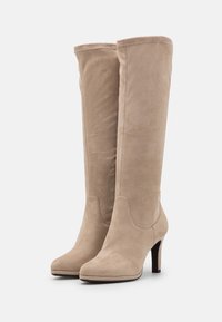 Stivali alti in suede beige con una texture liscia, punta rotonda e tacco a stiletto di 10 cm. Presentano cuciture per un tocco di dettaglio in più.