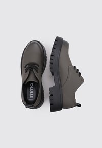 Zapatillas de goma verdes con puntera redonda, diseño con cordones, suela negra gruesa y una pestaña en el talón. El interior presenta el nombre de la marca.