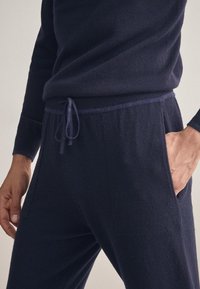 Mörkblå loungebyxor tillverkade av mjukt tyg, med elastisk midja och dragsko samt sidofickor. Slät textur genom hela byxorna.