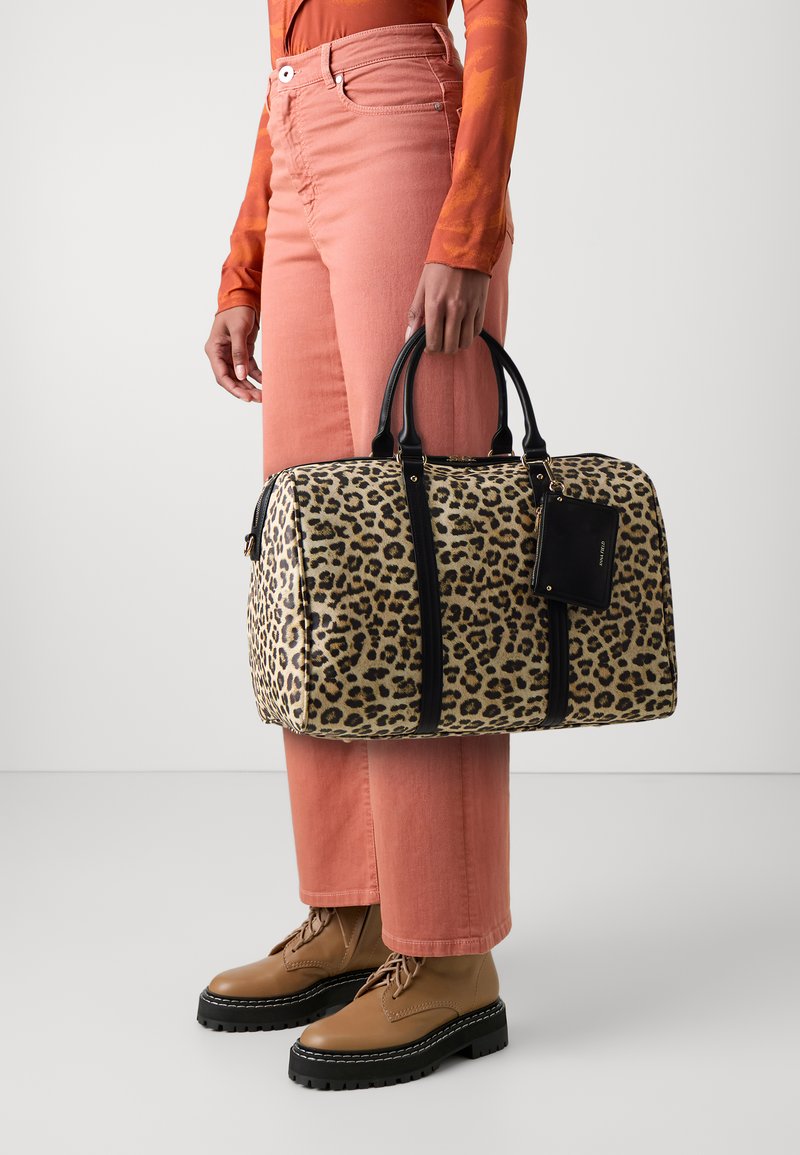 Torba sa leopard uzorkom, crnim detaljima, kožnim ručkama i oznakom za prtljagu. Uparena sa koralnim širokim hlačama i smeškim čizmama na vezivanje.