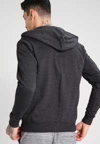 Dunkelgrauer Hoodie aus strukturiertem Material, mit einer Rückansicht, Kordelzugkapuze und gerippten Bündchen. Keine sichtbaren Logos oder Muster.