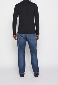 Svart långärmad tröja i kombination med blå denimjeans. Tröjan har rund halsringning och jeansen har en klassisk rak benmodell.