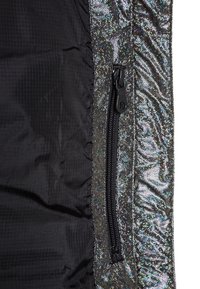 Zwarte lichtgewicht jas met een gestructureerde stof en een glanzend iriserend zijpaneel. Voorzien van een zak met rits. Details met metallic glans.