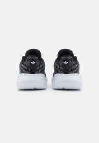 Sneakers neri in maglia con upper texture e suola in gomma bianca. Caratterizzati da un pull tab sul retro e un piccolo logo sul tallone.
