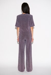 Paarse, sparkling jumpsuit met korte, brede mouwen, een fitted taille en wijde broekspijpen. Beschikt over een rits aan de achterkant en een gladde textuur.