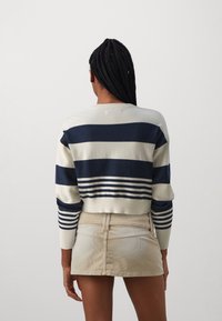 Pull court crème à rayures horizontales bleu marine avec poignets côtelés, assorti à une jupe en denim beige clair. La texture semble douce.