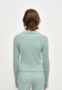 Ljust blått texturerat tröja med ett mjukt, fluffigt material, med en bred krage och åtsittande silhuett, matchat med byxor i samma färg.