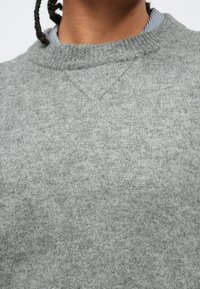 Gray knitted sweater with a ribbed crew neckline. The texture is soft, and fabric appears warm and lightweight, showing subtle variations in tone.