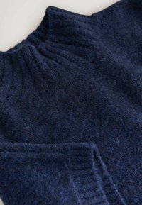 Dunkelblauer gestrickter Wollpullover mit geripptem Stehkragen und gerippten Bündchen, flach auf einer hellen Oberfläche ausgelegt.