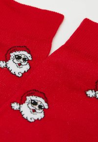 Rote gestrickte Socken mit einem Muster von Weihnachtsmann-Gesichtern, die Brillen und rote Hüte auf weißem Hintergrund tragen.