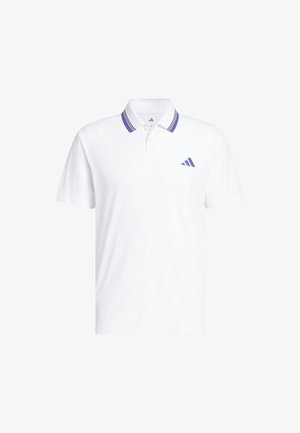 Junger Mann trägt weißes Poloshirt mit blau gestreiftem Kragen und dunkelblauer Hose, steht mit einer Hand in der Hosentasche.