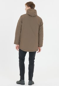 Brun puffjacka med huva, med en slät yta och en längre bakdel, kombinerad med svarta slim-fit byxor och grå stövlar.