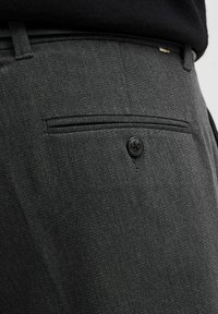 Pantalones grises a medida con una tela texturada, que cuentan con un bolsillo trasero y un cierre de botón negro para un almacenamiento seguro.