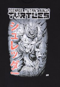 Svart t-shirt med en grå och vit grafisk av en muskulös rustad karaktär med röd japansk text och en stadsbild i bakgrunden.