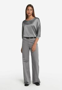 Blusa in satin grigia con scollatura ampia e maniche a tre quarti, abbinata a pantaloni dritti grigi chiari e una cintura nera.