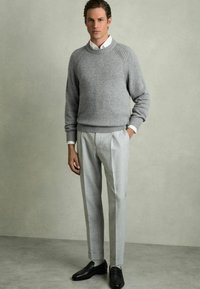 Grå stickad tröja med ribbad detaljering, i kombination med ljusgrå veckade byxor och svarta loafers. Slät tyg, skräddarsydd passform.