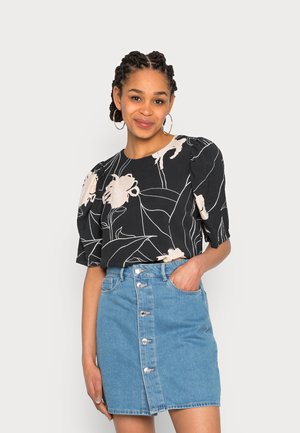 Blusa preta com padrão floral branco, mangas bufantes, combinada com uma saia de denim azul claro com fecho frontal em botão e bolsos.